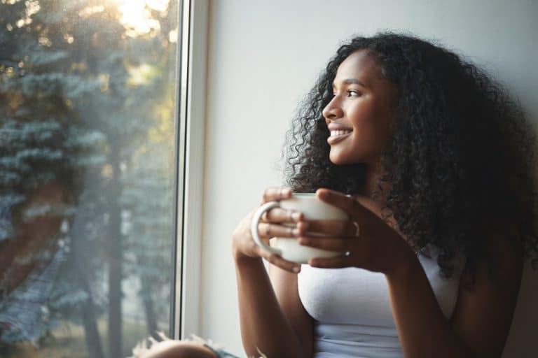 happy young lady looking out the window and enjoying coffee in the morning