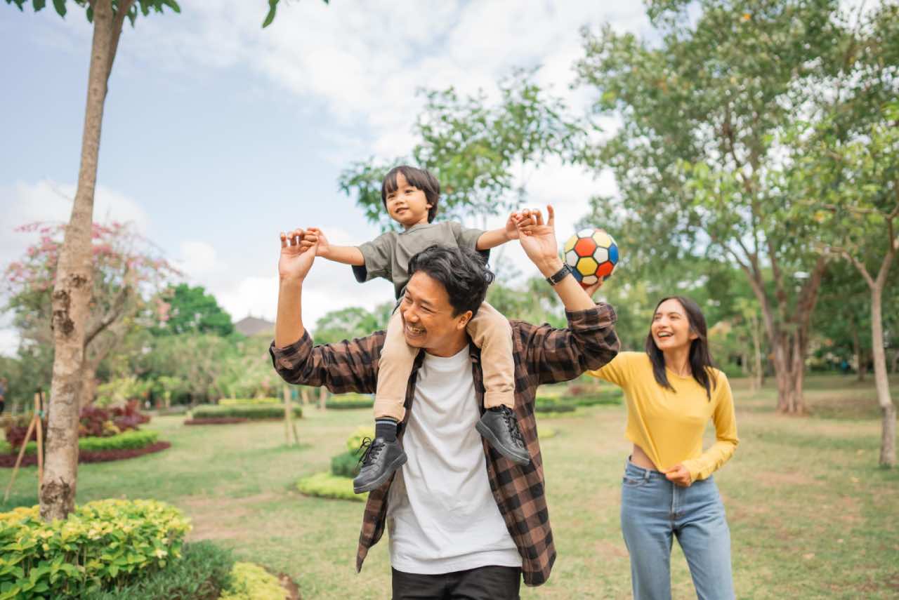 A happy family of three enjoying family time at a park showing close attachment of child with parents.